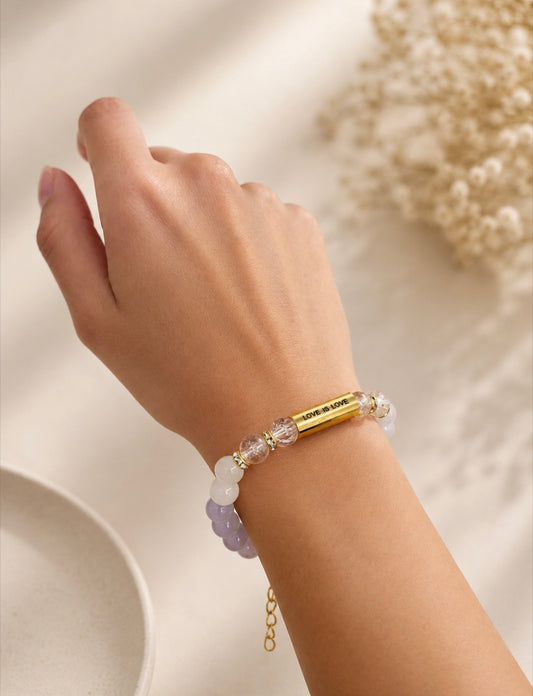 Close-up of Love Is Love Bracelet worn on wrist, showing gold engraved bar and crystal beads