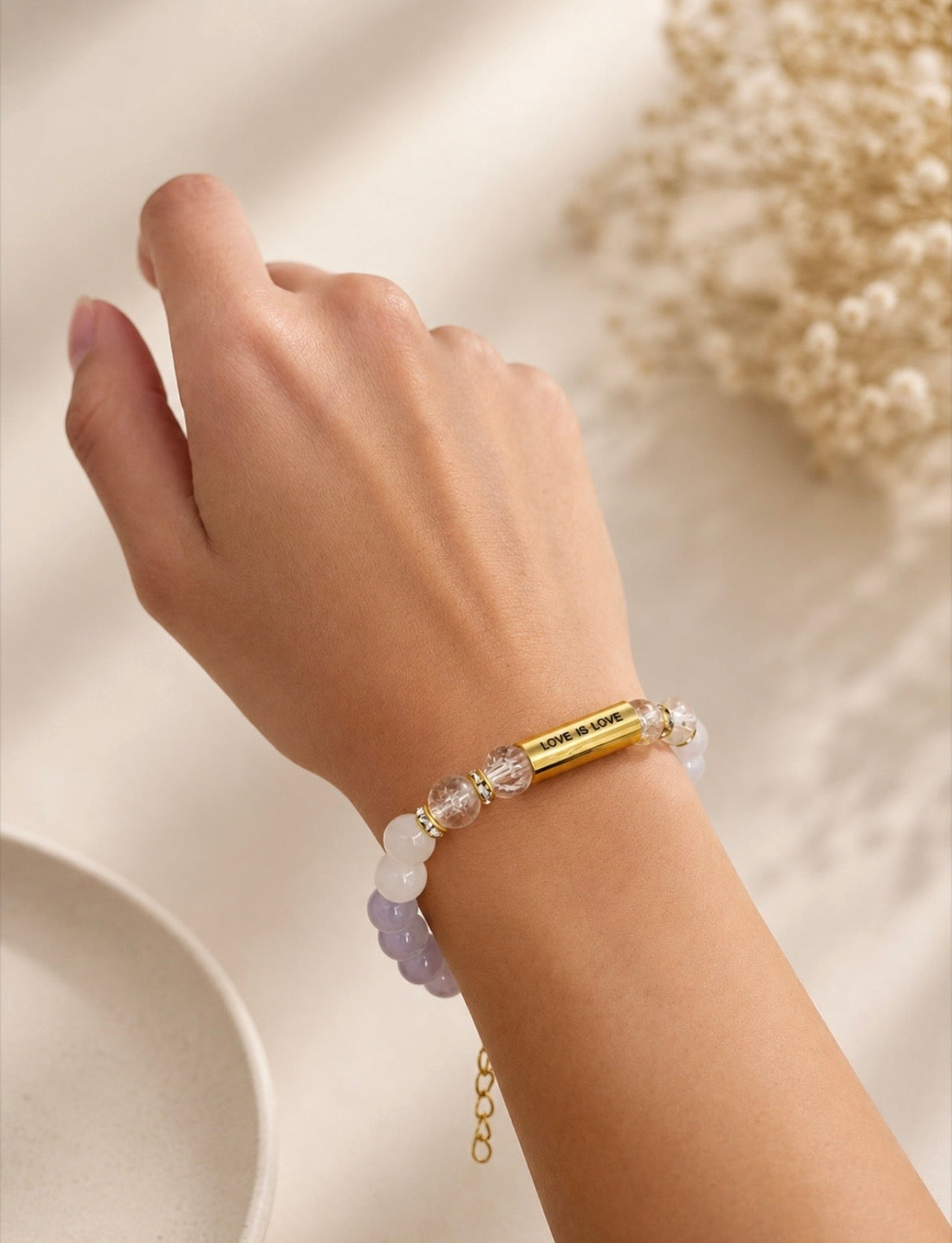 Close-up of Love Is Love Bracelet worn on wrist, showing gold engraved bar and crystal beads