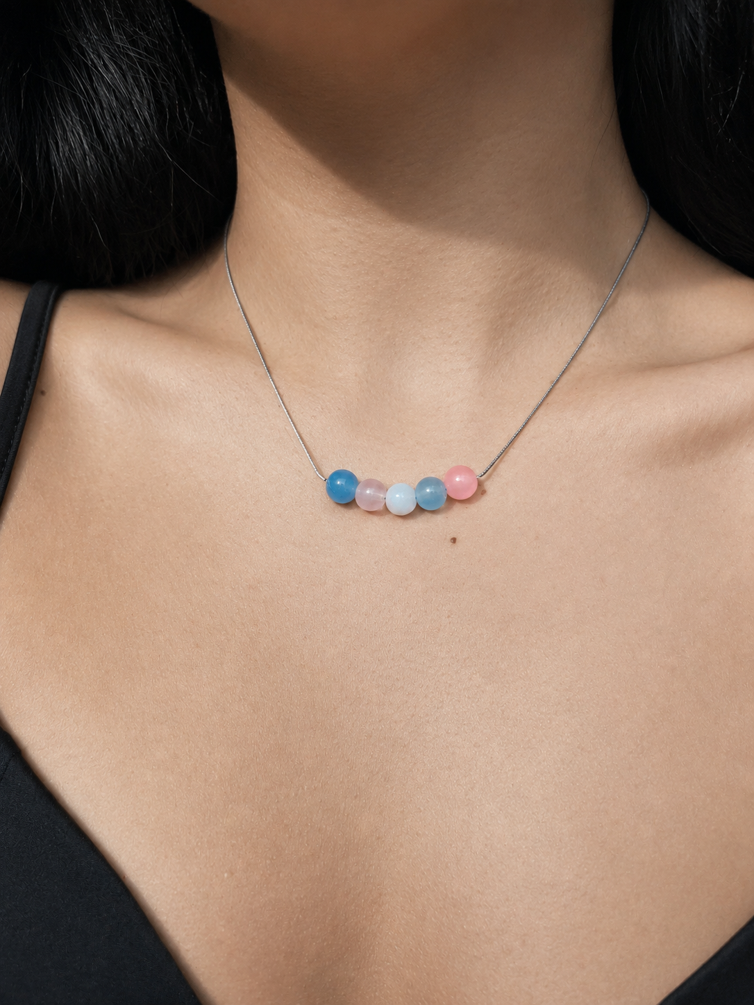 Close-up of The Alignment Trans Pride Necklace worn on a neckline showing pastel transgender pride bead colors